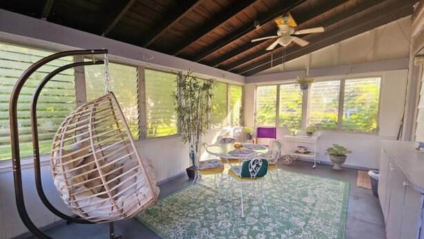 Una habitación iluminada por el sol con una silla colgante, una mesita y un ventilador de techo.