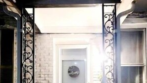 Un acceso cubierto con una puerta blanca, un cartel de bienvenida y plantas en macetas.