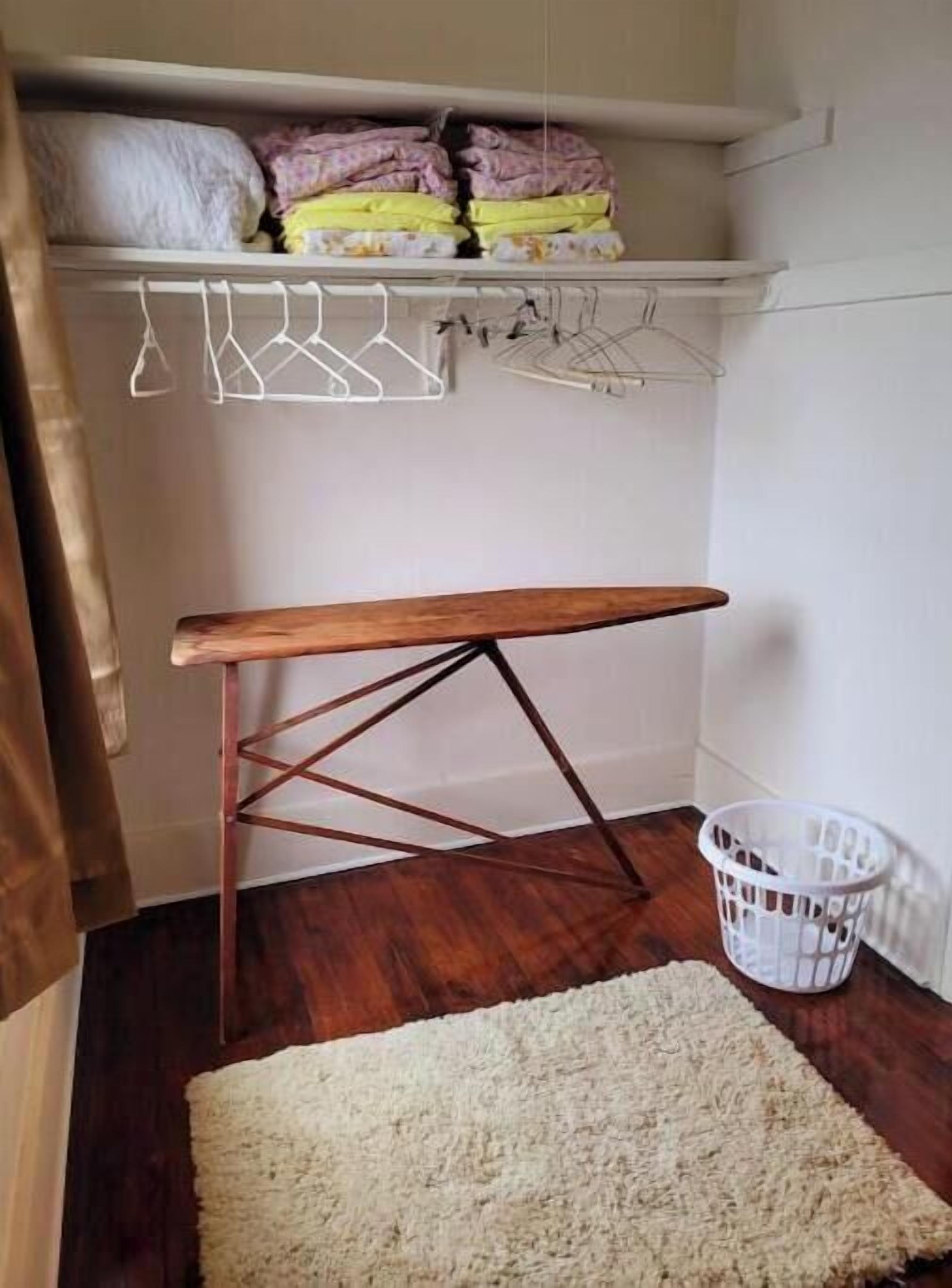 A room with a wooden bench, a white rug, a laundry basket, and a shelf with folded blankets.