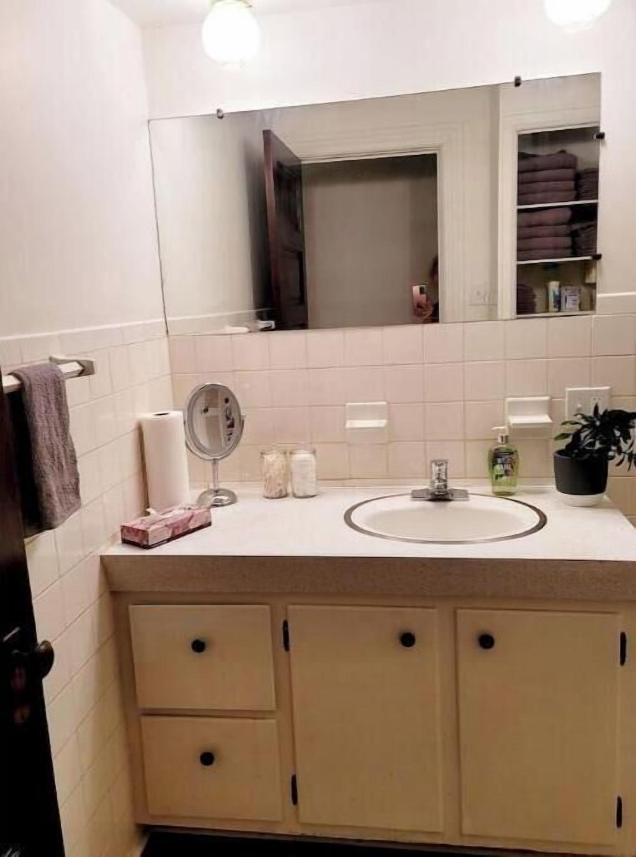 Un baño con lavamanos blanco, espejo y dos armarios con cajones.