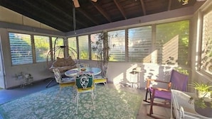 Una habitación luminosa con ventilador de techo, ventanas amplias, una mesa redonda y varias sillas.
