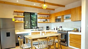 A modern kitchen with wooden beams, a central island, and a dining area with four chairs. - House of the Baobas! "Your home in the nature of Atitlán". (San Juan La Laguna)