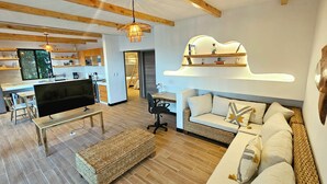 A modern living room with a TV, sofa, and wooden furniture. There is a kitchen area with a dining table and chairs. - House of the Baobas! "Your home in the nature of Atitlán". (San Juan La Laguna)