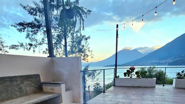 Ein Steinkamin mit Flammen, eine Couch und ein Balkon mit Blick auf einen Berg und einen See.