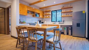 Eine moderne Küche mit Holzschränken, einer zentralen Kochinsel mit Stühlen, einem Edelstahlkühlschrank und einem Fenster, das natürliches Licht hereinlässt.