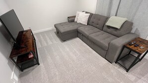 A living room with a sectional sofa, a TV on a wooden stand, and a small table with remotes. - Modern Comfort | Private Guest Suite Getaway (Cochrane)