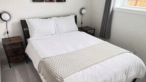 A bedroom with a bed, nightstands, a wall-mounted lamp, and a window with curtains. - Modern Comfort | Private Guest Suite Getaway (Cochrane)