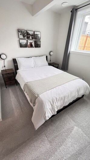 A bedroom with a bed, nightstands, a wall-mounted lamp, and a window with curtains.
