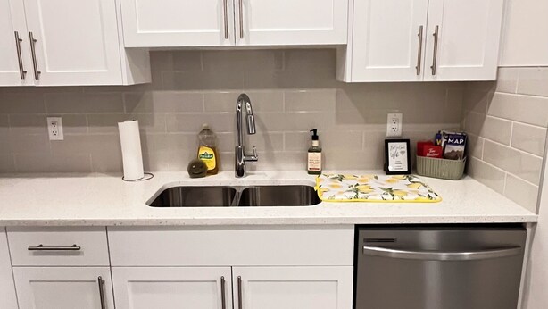 A kitchen with white cabinets, a stainless steel dishwasher, and a tiled backsplash. - Modern Comfort | Private Guest Suite Getaway (Cochrane)
