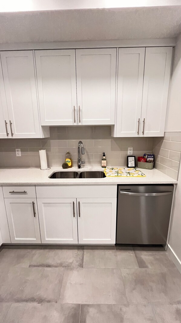 A kitchen with white cabinets, a stainless steel dishwasher, and a tiled backsplash.