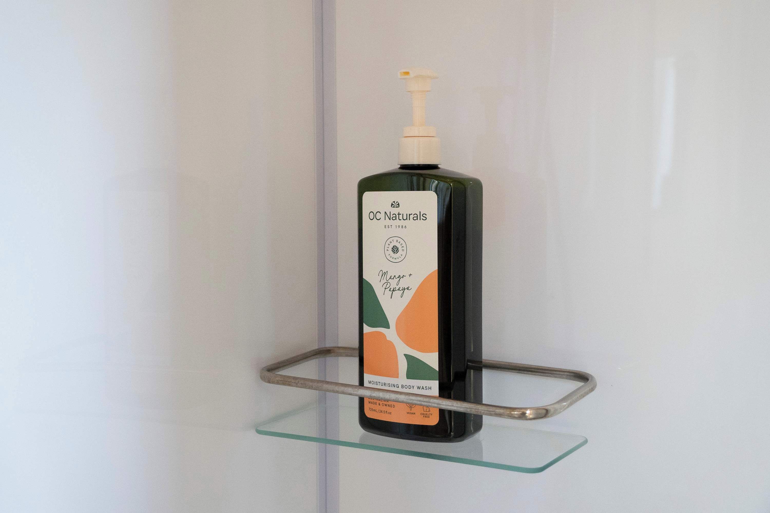 Een fles OC Naturals douchegel op een glazen plank.