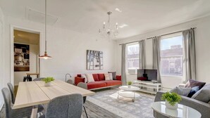 A modern living room with a dining area, a red sofa, a TV, and large windows. - Mont-Royal Apartment & Suite Near La Fontaine Park (Montreal)