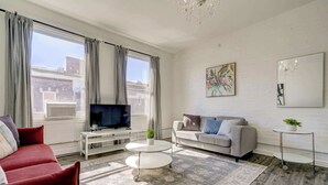 A modern living room with a red sofa, grey sofa, and a white coffee table. There is a TV on a white stand, a small plant, and a painting on the wall. - Mont-Royal Apartment & Suite Near La Fontaine Park (Montreal)
