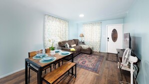 Una sala de estar con un sofá, una mesa de comedor dispuesta con platos y vasos, una lámpara y un ventilador.