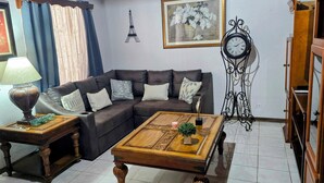 A living room with a brown leather sofa, a wooden coffee table, a side table with a lamp, a clock, and a wall with a picture of the Eiffel Tower. - Cozy 3 bedroom House in Quepos center and near Manuel Antonio National Park (Quepos)