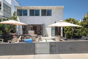Una casa moderna de dos pisos con un patio que incluye mobiliario exterior y sombrillas.