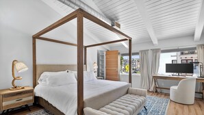 A modern bedroom with a four-poster bed, a desk with a computer, and a view of the city.
