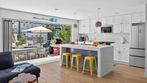 A modern kitchen with white cabinets, a central island with stools, and a view of an outdoor patio area.