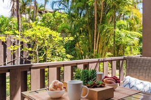 Una terraza de madera con una silla de mimbre, una mesa con un cuenco de fruta, una taza y una hogaza de pan.