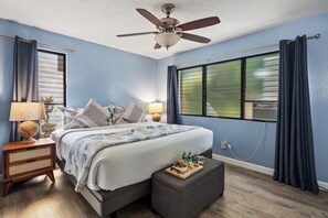 Un dormitorio con cama, lámparas de noche, ventilador de techo, ventana con cortinas y mesita de noche con lámpara.