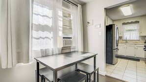 Una cocina con armarios blancos, un refrigerador negro y una ventana con cortinas de gasa.