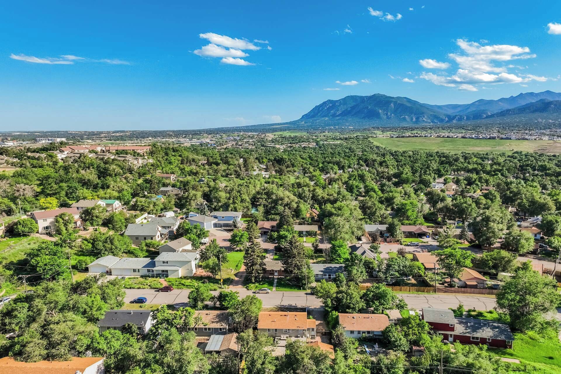 A residential area with houses surrounded by dense greenery and mountains in the background.
