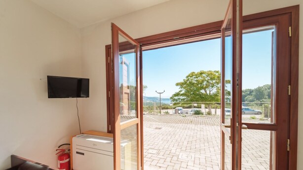 A room with a bed, a small table, a television, and a window with a view of a parking area and trees.