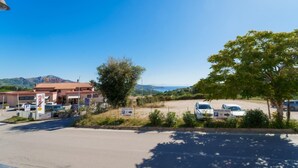 A parking area with a building labeled 'CONAD' and a view of the sea and mountains in the background.