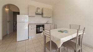 Een compacte keuken met een koelkast, fornuis en kastjes. Er is een eettafel met stoelen en een klein eiland.