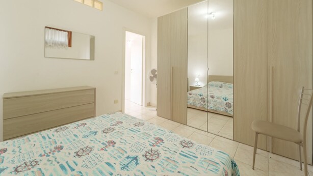 Een slaapkamer met een bed, een stoel, een kledingkast en een spiegel.