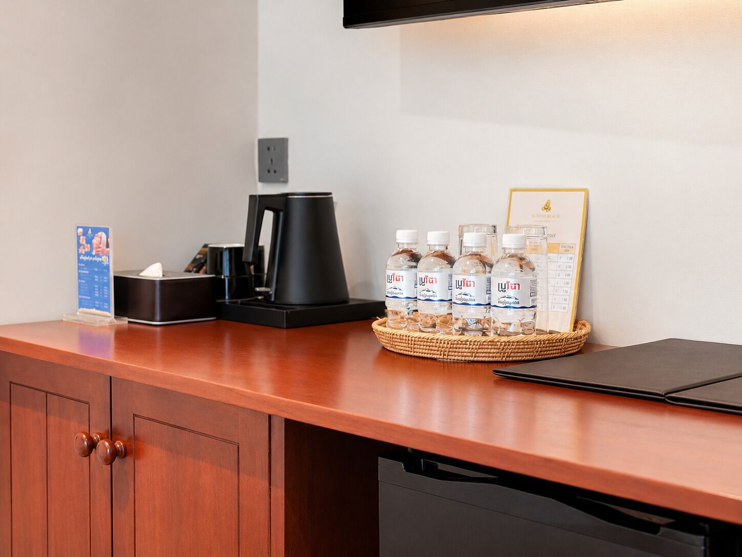 Ein Hotelrezeptionstresen mit Kaffeemaschine, Wasserflaschen, Taschentuchbox und einem gerahmten Menü.