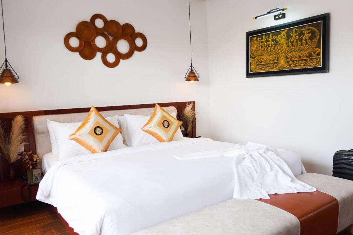 Una cama bien tendida con sábanas blancas y almohadas decorativas, un cabecero de madera y una obra de arte colgada en la pared.