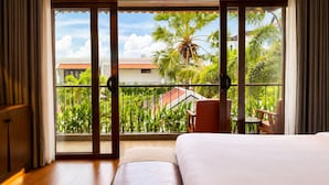 A hotel room with a large bed, a balcony with a view of greenery and a building, and a wooden floor. - Happy Resort Siem Reap (Siem Reap)
