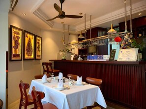 A restaurant with a dining table set for two, a bar area, and framed artwork on the wall.