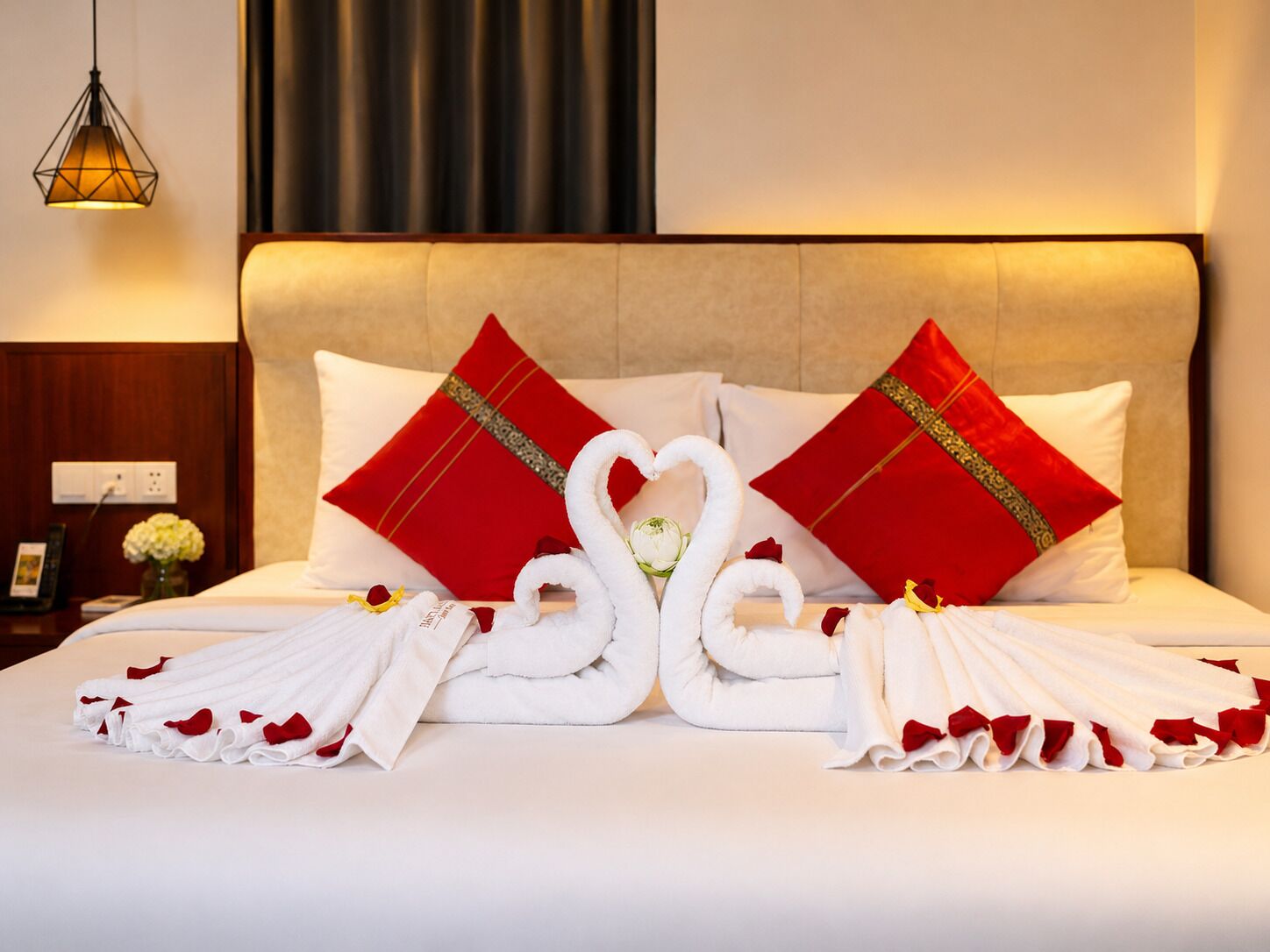 A hotel room with a bed, red pillows, white towels, and a swan-shaped towel arrangement.