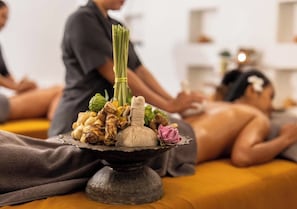 Une séance de massage thérapeutique utilisant diverses herbes et agrémentée d’une fleur, le tout présenté sur un plateau.