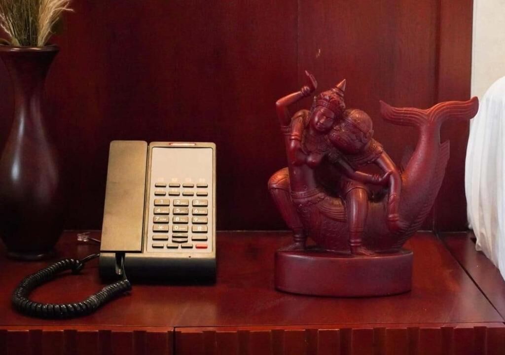 A wooden desk with a telephone, a vase with dried plants, and a statue of a figure.
