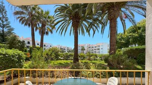A round table with chairs on a balcony with a yellow railing, overlooking a garden with palm trees and a building in the background. - Rustic and peaceful with pool (Lagos)