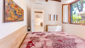 Un dormitorio con cama, un cuadro, un reloj, una ventana y una puerta que da a otra habitación.