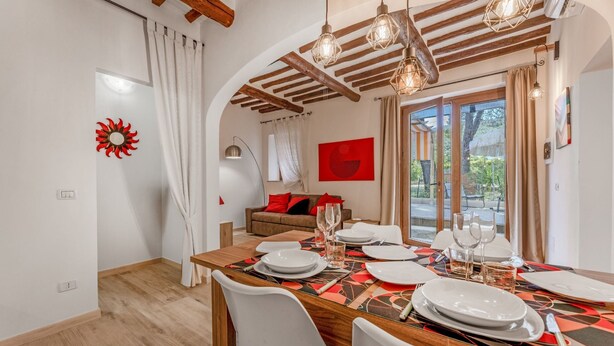 Comedor con una mesa de madera dispuesta para cuatro personas, sillas blancas y un cuadro abstracto rojo en la pared.