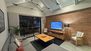 Un salon moderne avec un grand téléviseur, une table basse en bois, un canapé et un mur décoratif en briques.