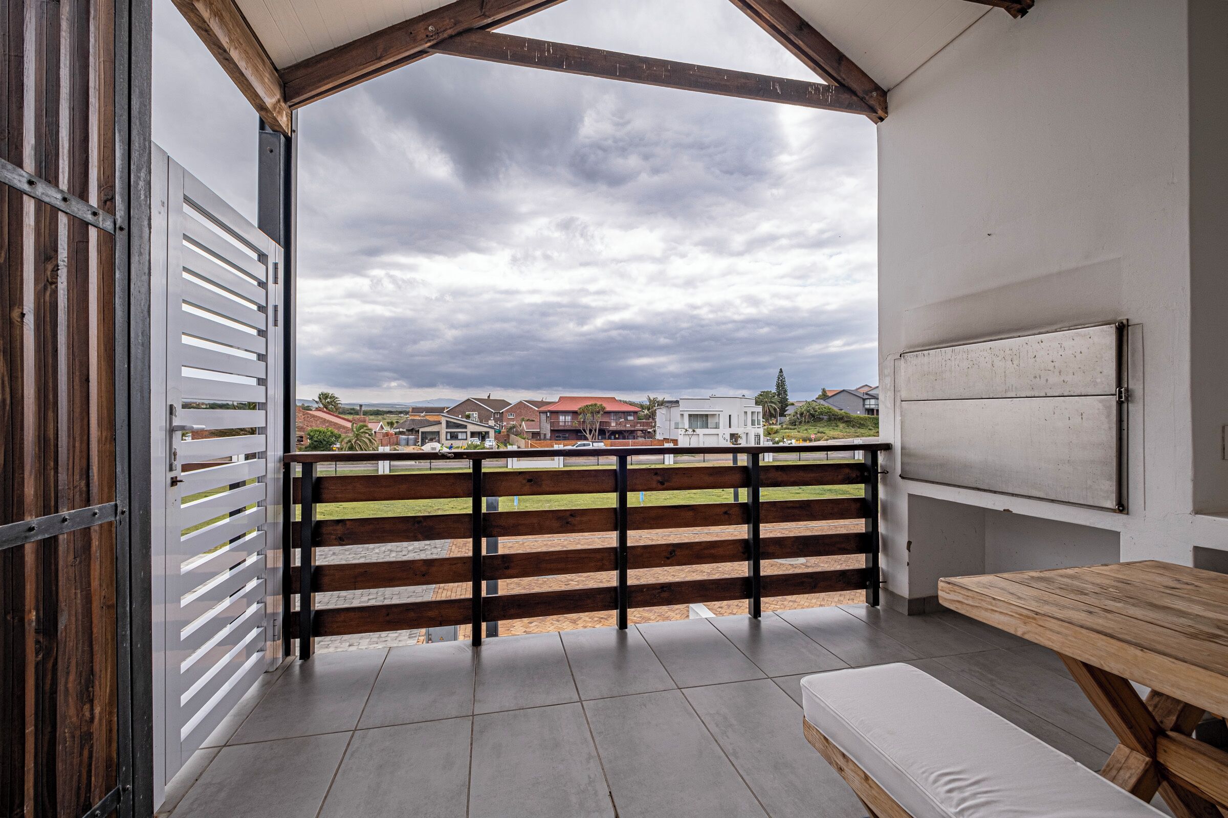 Een balkon met houten hekwerk, een bankje en een uitzicht op huizen in de verte.