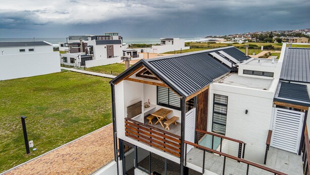 Un immeuble résidentiel moderne doté d’un balcon, offrant une vue sur la mer et surplombant un ciel nuageux.