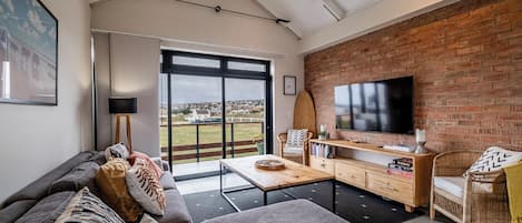 A modern living room with a large TV, comfortable seating, and a view of the outdoors.