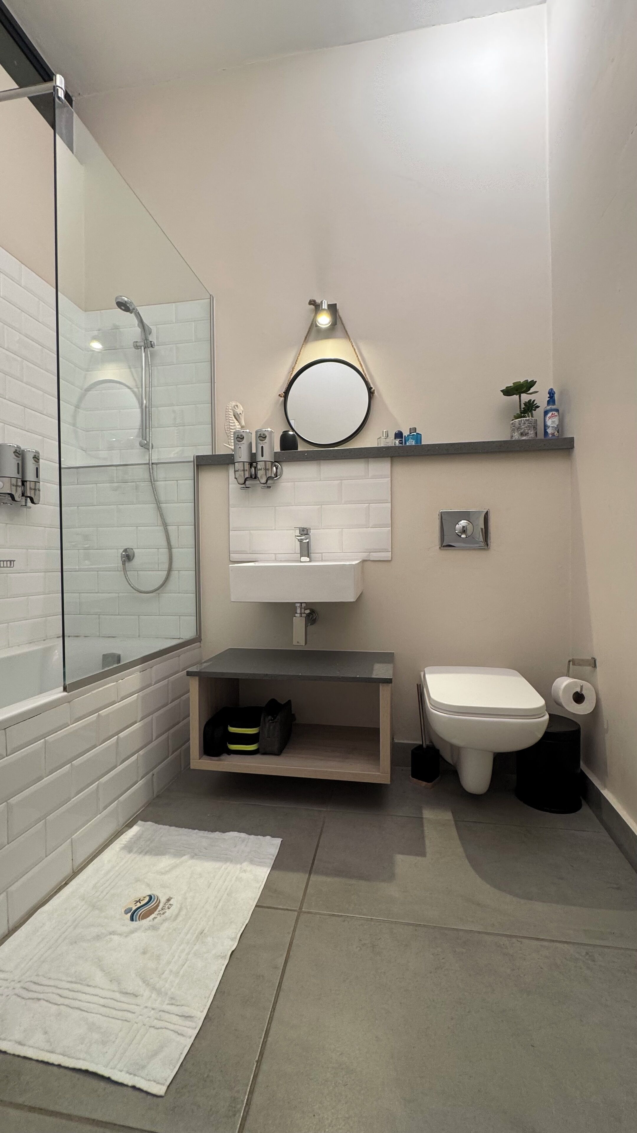 A modern bathroom with a glass-enclosed shower, a white sink, a toilet, and a small shelf with toiletries.