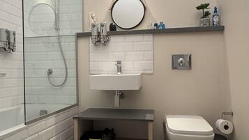 A modern bathroom with a glass-enclosed shower, a white sink, a toilet, and a small shelf with toiletries.