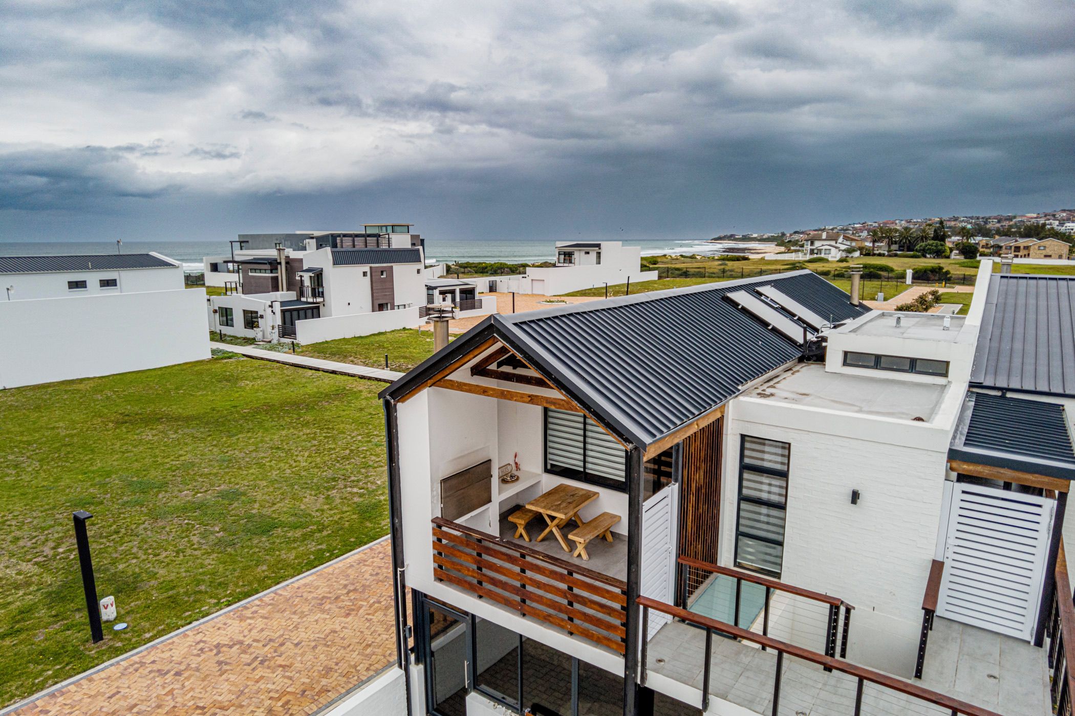 Une maison moderne dotée d’un balcon, offrant une vue sur la mer et disposant d’une cour gazonnée.