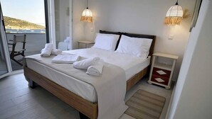 A modern bedroom with a large bed, two bedside tables, a view of the sea, and a balcony.