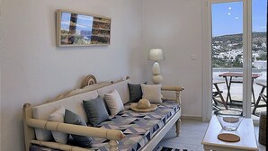 A cozy bedroom with a bed, a bedside table, a lamp, and a window with a view of the sea.