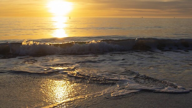 Een strand bij zonsondergang, met golven die de kust naderen.